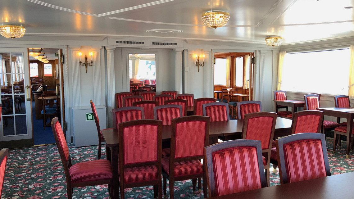 Dampfschiff Stadt Luzern - Queens Salon Queens Salon von dem Dampfschiff Stadt Luzern mit rot gepolsterten Stühlen und einem blumigen Teppich.