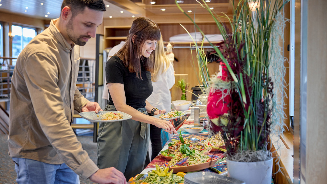 Gäste vom Thai-Schiff sehen zu, wie der Koch auf dem Thai-Schiff am Buffet das Essen zubereitet