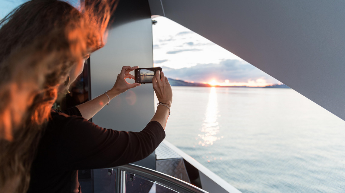 Sonnenuntergang ist Foto-Zeit Sonnenuntergang auf dem Schiff. Eine junge Frau schiesst ein Foto mit ihrem Mobiltelefon