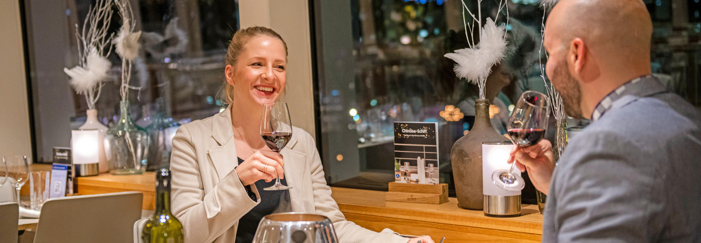 Paar stosst die Weingläser an. Der Tisch ist mit Fondue Chinoise gedeckt