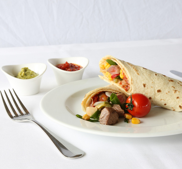 Ein Teller auf weiss gedecktem Tisch mit leckeren Fajitas