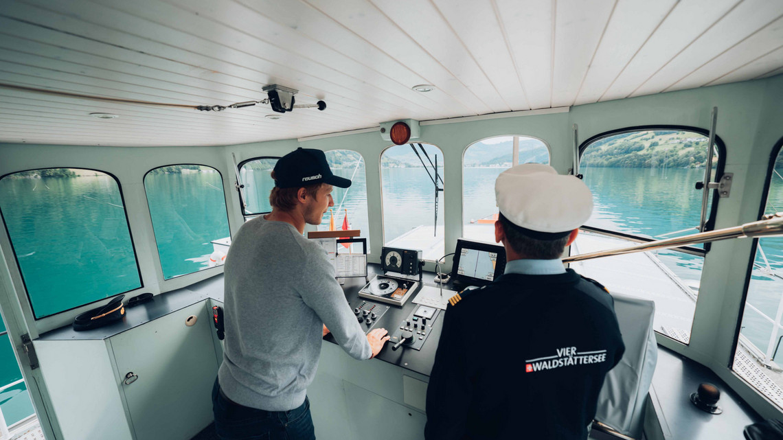 Marco Odermatt steht links neben dem Kapitän im Steuerhaus, schaut auf die Karte und stützt sich ab.