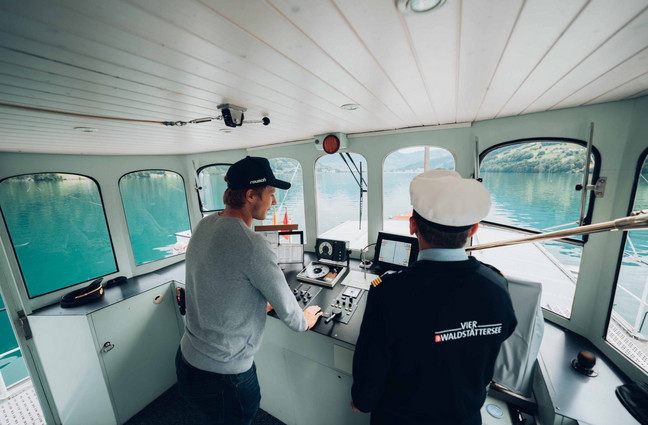 Skirennfahrer Marco Odermatt Marco Odermatt steht links neben dem Kapitän im Steuerhaus, schaut auf die Karte und stützt sich ab.