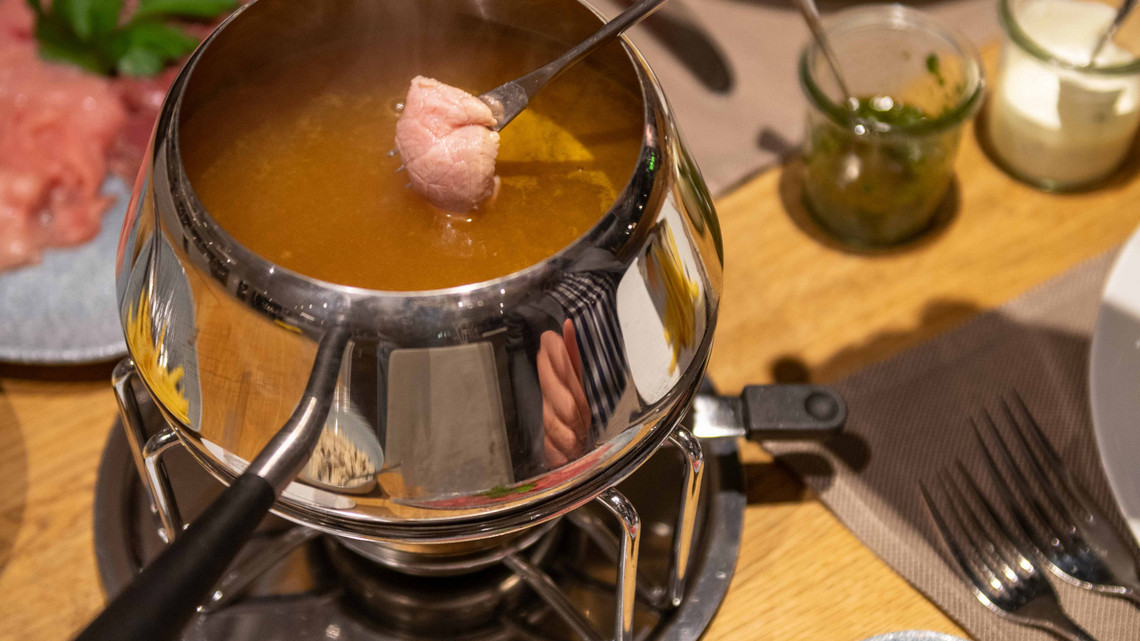 Fleisch im Fondue Chinoise Caquellon Ein Stück Fleisch wird im Caquellon