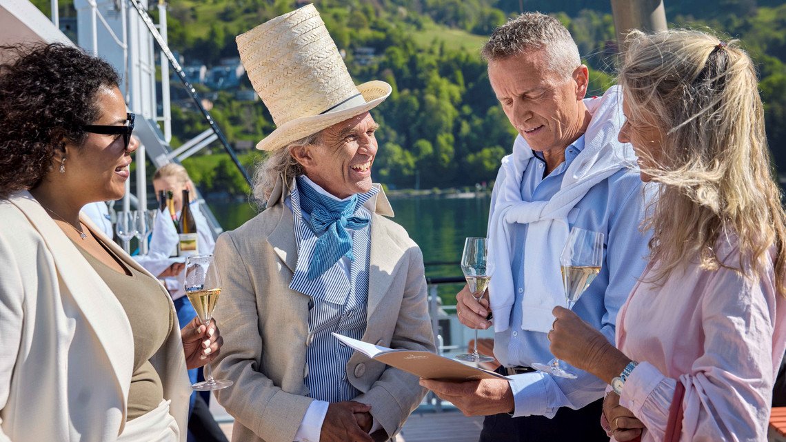 Eine Gruppe von Menschen stehen im Kreis draussen und sprechen miteinander und trinken ein Glas Champagner.